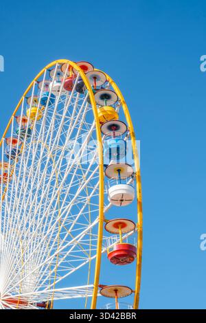 Vue verticale en gros plan d'une grande roue colorée contre un ciel bleu clair par une journée lumineuse et ensoleillée Banque D'Images