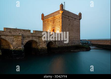 Gros plan photo nocturne longue exposition du Castelo Real illuminé reflétant les eaux calmes du port d'Essaouira, au Maroc. Banque D'Images
