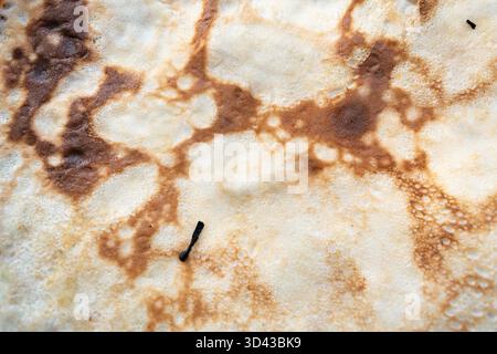 Gros plan macro détaillé de la surface irrégulière d'une crêpe, avec des motifs brun doré et légèrement brûlés. Symbolise la nourriture de réconfort, la cuisine maison, et Banque D'Images