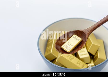 Délicatement creuser des lingots d'or avec une cuillère dans un bol en céramique bleu et blanc sur un fond blanc propre, symbolisant la richesse, le luxe, la prospérité Banque D'Images