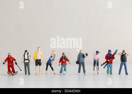 Figurines miniatures de personnes engagées dans diverses activités de plein air sur un fond minimal Banque D'Images