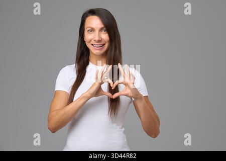 Femme souriante faisant une forme de coeur avec des doigts exprimant le bonheur et l'amour Banque D'Images