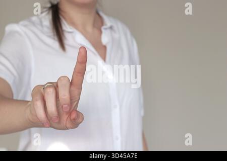 Femme en chemise blanche montrant un index relevé, symbolisant un avertissement, une restriction ou une instruction importante. Concept d'attention, de prudence et de com Banque D'Images