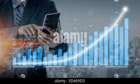 Un homme d'affaires interagit avec son smartphone, analysant les données financières affichées sur fond d'un graphique en pleine croissance et d'un horizon urbain. L'image Banque D'Images