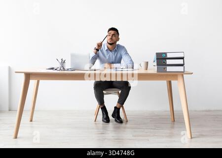 Homme arabe concentré travaillant sur ordinateur portable au bureau à domicile tout en contemplant des idées Banque D'Images