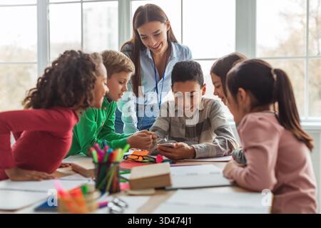 École multiethnique enfants et enseignant s'engageant avec smartphone dans un cadre de salle de classe moderne Banque D'Images