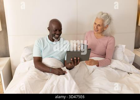 Regardant la tablette, homme senior afro-américain et femme assis dans la chambre, tenant une tasse grise Banque D'Images