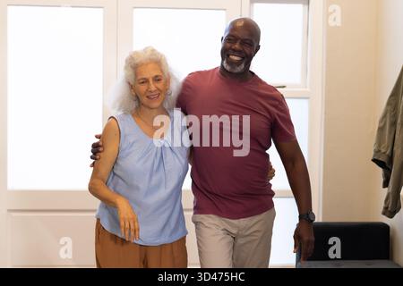 Embrasser divers couples seniors marchant dans l'entrée, avec porte en verre dépoli, banc et veste Banque D'Images