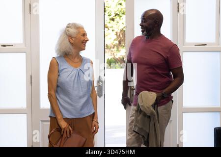Couple senior debout discutant dans l'entrée de la maison, avec sac à main en cuir marron et veste légère Banque D'Images