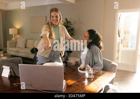 Enregistrement de diverses amies féminines collaborant dans le studio du salon, avec ordinateur portable et microphones Banque D'Images
