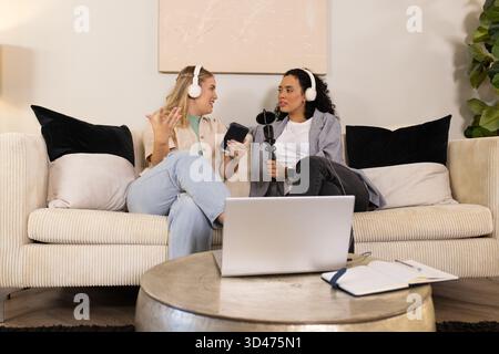 Enregistrement podcast, diverses amies de sexe féminin discutant sur le canapé dans le salon avec microphone pour ordinateur portable Banque D'Images