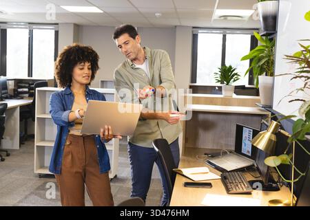 Collaboration de divers collègues examinant les données sur ordinateur portable dans un bureau ouvert, avec des marqueurs colorés Banque D'Images