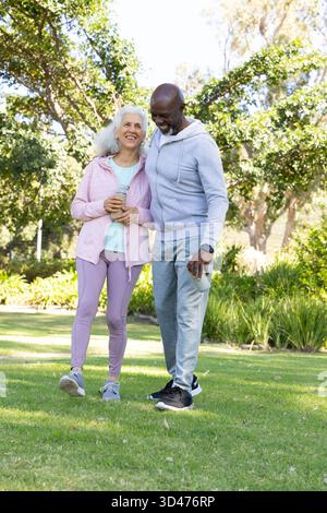 Marchant divers couple senior tenant une bouteille d'eau réutilisable et thermos en acier inoxydable dans le parc Banque D'Images
