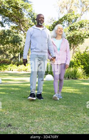 Marchant divers couples de personnes âgées tenant la main sur la pelouse du parc paysager, avec des lumières de jardin blanches Banque D'Images