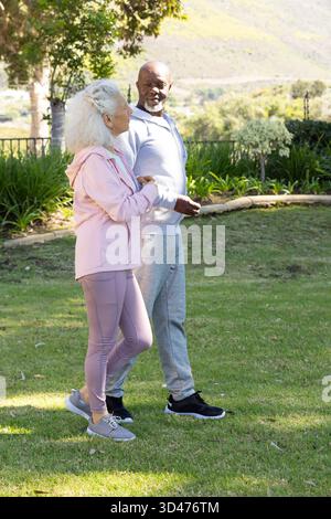 Marchant divers couples seniors discutant sur la pelouse herbeuse dans le jardin de l'arrière-cour, partageant une promenade paisible Banque D'Images