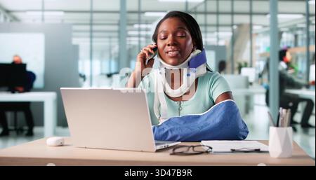 Femme souriant avec bras cassé au bureau, ordinateur toujours allumé. Banque D'Images