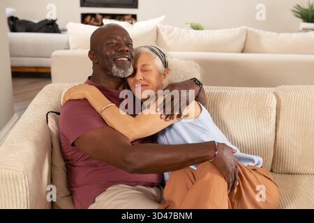 Embrassant un couple diversifié se penchant ensemble sur un canapé velours côtelé dans le salon, avec des œuvres d'art encadrées Banque D'Images