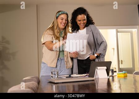 Debout diverses collègues féminines examinant des documents imprimés dans un espace de travail moderne, avec ordinateur portable Banque D'Images