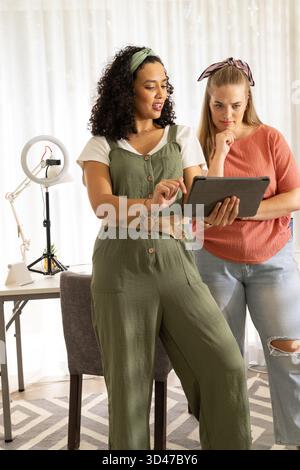 Discuter du contenu, diverses amies féminines collaborant dans le home studio avec tablette, lumière annulaire LED Banque D'Images