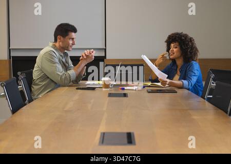 Discuter des ordinateurs portables et des papiers, divers collègues collaborant dans la salle de réunion, avec tasse à café Banque D'Images