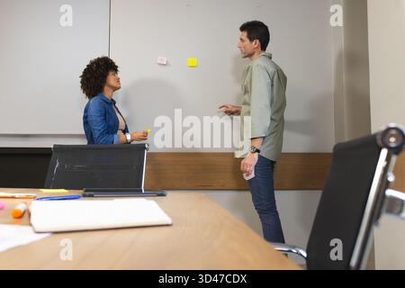 Divers collègues discutent des idées, placent des notes adhésives sur le tableau blanc dans la salle de réunion, avec un ordinateur portable Banque D'Images