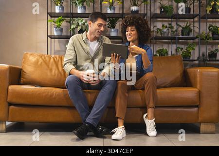 Discuter de divers collègues assis sur le canapé en cuir dans le salon, avec tablette et tasse à café Banque D'Images