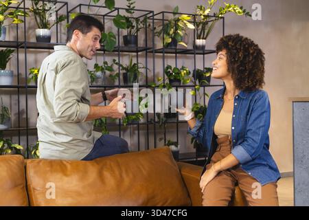 Bavardez divers amis assis sur le canapé en cuir marron dans le salon, avec des tasses en céramique foncée Banque D'Images