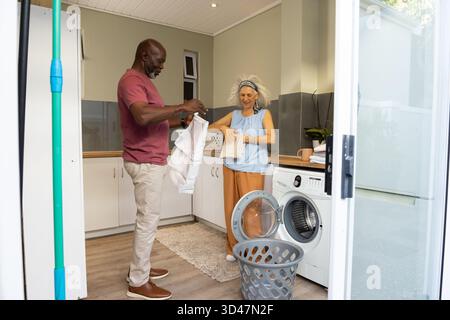 Linge pliant divers couple senior dans une salle de lavage à la maison lumineuse, avec panier et serviettes pliées Banque D'Images