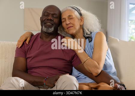 Relaxant couple senior diversifié se blottissant sur canapé léger dans le salon, avec peinture abstraite Banque D'Images