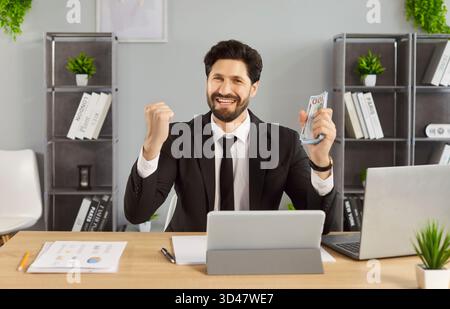 Heureux homme d'affaires réussi dans le bureau, homme assis au bureau, tenant l'argent comptant, souriant Banque D'Images