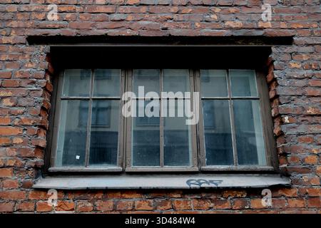 Fenêtre en bois à plusieurs vitres altérées dans un mur de briques rouges avec mortier usé et graffiti sur le seuil, photographiée à Helsinki, Finlande, en plein jour. Banque D'Images