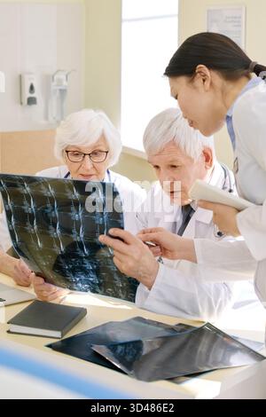 Groupe de médecins expérimentés examinant la radiographie du patient après examen IRM et analysant les résultats ensemble dans la salle de consultation Banque D'Images