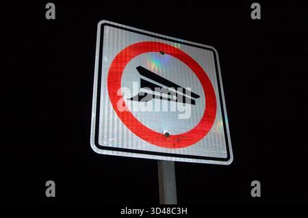 Panneau de signalisation réfléchissant la nuit montrant un cercle rouge avec un symbole de rampe de bateau, illuminé contre un ciel sombre Banque D'Images