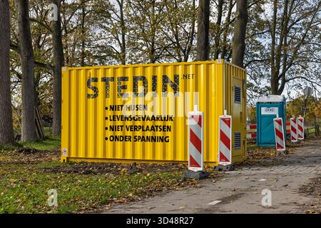 Conteneur Stedin jaune avec avertissements de danger en néerlandais (« danger pour la vie », « sous-tension ») placé dans une zone boisée pendant les travaux de construction. Banque D'Images