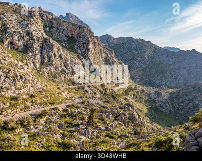 Route sinueuse à sa Calobra, Majorque, route de montagne sinueuse serpente à travers un terrain accidenté et rocheux avec une végétation verte, sur fond de pics imposants sous un ciel bleu clair, Majorque Banque D'Images