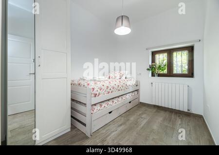 Composition d'une chambre minimaliste montrant une couette blanche parfaitement nichée et, au contraire, un vase en verre avec des tulipes rouges sur une table de nuit en métal Banque D'Images