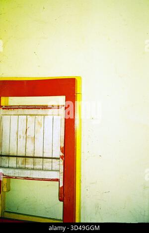Chaise pliée en bois rouge appuyée contre un mur jaune, photo de film analogique avec une composition simple et des tons chauds. Banque D'Images