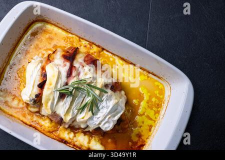 Savoureux poulet cuit au four garni de bacon, de camembert fondu et de romarin frais, prêt à servir Banque D'Images