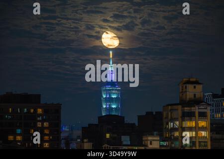 New Taipei City, Taiwan - 15 juin 2025 : une lune se lève de façon spectaculaire derrière le gratte-ciel illuminé Taipei 101 la nuit. Fenêtres éclairées de l'appartement Ar Banque D'Images