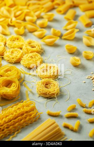 Variété de formes de pâtes jaunes non cuites dispersées sur un fond bleu clair Banque D'Images