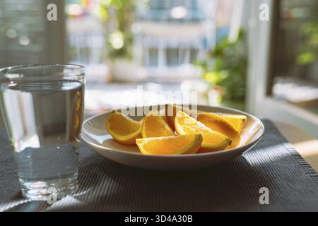 Régime mono orange. tranches d'orange pelées sur assiette et verre d'eau propre dans le verre sur la table, dans les rayons du soleil Banque D'Images