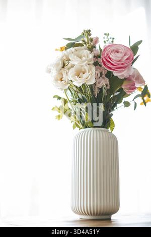 Un bouquet coloré de fleurs de différentes formes et tailles orne un vase blanc côtelé Banque D'Images