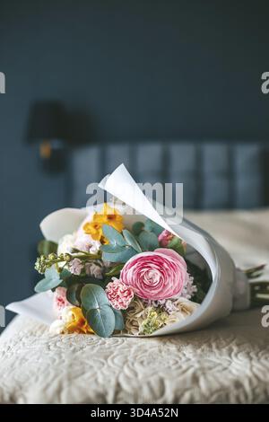 Un bouquet vibrant de fleurs reposant sur un lit soigneusement fait, avec pour toile de fond un cadre de chambre élégant, évoquant un sentiment de fraîcheur et d'élégance Banque D'Images