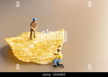 Personnes miniatures : les travailleurs travaillent avec des chips de pomme de terre Banque D'Images
