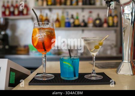 Crema, Italie - 25 août 2025 trois cocktails rafraîchissants colorés servis sur un comptoir de bar avec un fond flou de bouteilles et d'équipement de bar pro Banque D'Images
