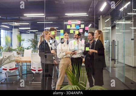 Brainstorming de l'équipe d'affaires au bureau, en utilisant des notes adhésives sur le mur de verre tout en discutant des stratégies. Banque D'Images