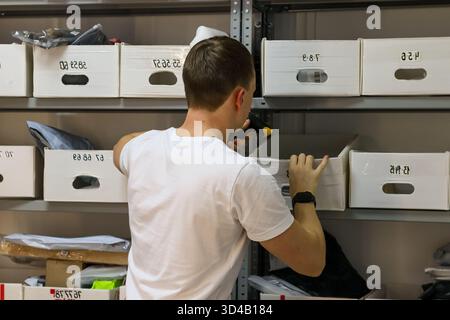 Le travailleur scanne et cherche la boîte sur l'étagère au point de ramassage. Vue arrière de l'homme en chemise blanche à l'aide du scanner et de la main pour accéder à la boîte étiquetée sur métal Banque D'Images