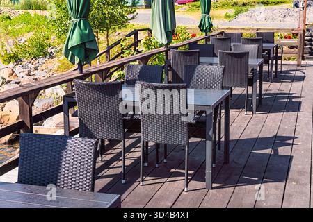 Terrasse de restaurant vide en plein air par une journée ensoleillée à Axmar, en Suède, avec des rangées de chaises en osier sombre, des tables et des parasols pliés verts, invitant RELA Banque D'Images