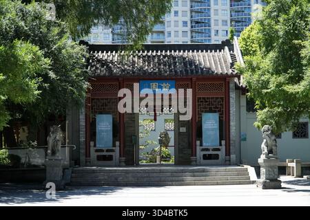 Jardin chinois de l'amitié. Porte d'entrée avec architecture traditionnelle, statues de lion en pierre et bâtiments de ville modernes en arrière-plan, Sydney, au Banque D'Images