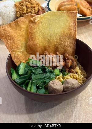 Mie Ayam Bakso, un restaurant de rue indonésien populaire, propose des nouilles jaunes garnies de poulet savoureux, boulettes de viande, légumes verts et wontons frits croustillants dans un Banque D'Images